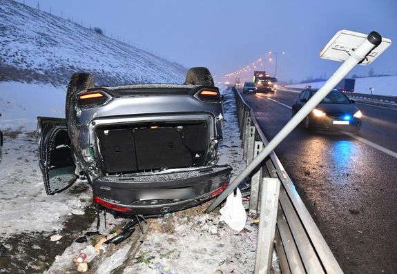 Uszkodzony pojazd w wyniku dachowania na autostradzie. W tle policyjny pojazd z włączonymi sygnałami świetlnymi