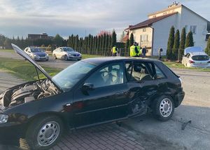 Samochód koloru ciemnego z uszkodzoną karoseria znajduje się na poboczu drogi.