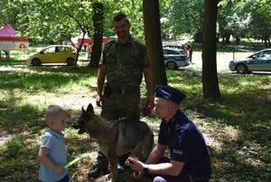 Chłopczyk obok którego stoi pies. Obok psa jest policjant i funkcjonariusz Straży Granicznej