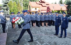 Policjant składa kwiaty przy pomniku. W tle policjanci