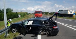 Samochód na psie ruchu. Pojazd posiada uszkodzenia w wyniku wypadku. Przed pojazdem stoi policjant.