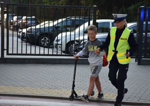 Policjantka przez przeprowadza przez przejście dla pieszych chłopca z hulajnogą