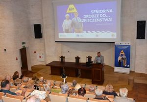 Aula wykładowa. Mężczyzna prowadzi prelekcję. Na sali znajdują się seniorzy.