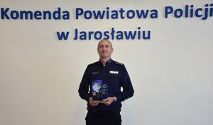 Policjant trzyma w ręce statuetkę. W tle napis o treści Komenda Powiatowa Policji w Jarosławiu