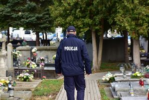 Policjant przechodzi przez alejkę cmentarną