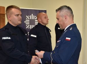 Policjant wręcza nowemu funkcjonariuszowi odznakę i legitymację