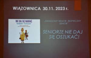 Slajd na którym widnieje napis o treści Wiązownica 30.11.2023 r. oraz &quot;Bezpieczny senior-jak nie dać się oszukać. Po lewej stronie znajduje się grafika dot. oszustw seniorów.