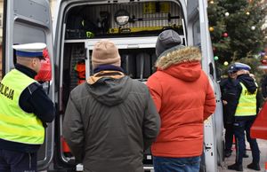 Mężczyźni w obecności policjanta oglądają radiowóz