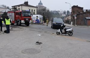 Skrzyżowanie dróg, miejsce kolizji drogowej. Na zdjęciu widoczny jest uszkodzony motorower. W tle samochód osobowy. Po lewej stronie znajdują się policjanci.