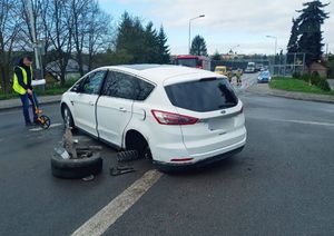 Uszkodzony samochód na jezdni. Przy nim policjant prowadzący czynności oględzin.