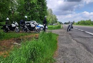 Droga. Na poboczu stoi radiowóz oraz dwa motocykle. Przy drodze znajduje się policjant. Na drodze stoi motocykl.