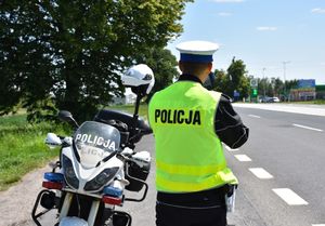 Policjant mierzy prędkość kierującemu pojazdem. Obok funkcjonariusza znajduje się motocykl.