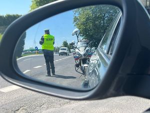 W lusterku samochodu odbija się policjant który mierzy prędkość przejeżdżającemu pojazdowi