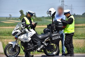 Policjanci w trakcie kontroli kierującego pojazdem. Obok nich stoi policyjny motocykl