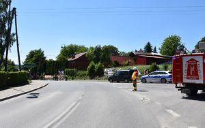 Skrzyżowanie dróg. Po prawej stronie stoi policjant. W tle zakręt