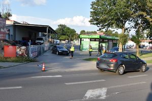 Miejsce zdarzenia drogowego. W tle samochód osobowy. Przed nim znajdują się policjanci.