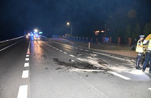 Miejsce wypadku drogowego. Pora nocna. Po prawej stronie znajdują się policjanci. W tle samochody.