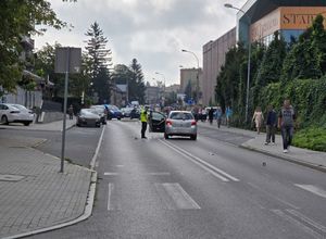 Miejsce wypadku drogowego. Za przejściem dla pieszych znajduje się samochód oraz policjant