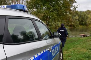 Radiowóz. Przed nim policjantka. W tle rzeka.