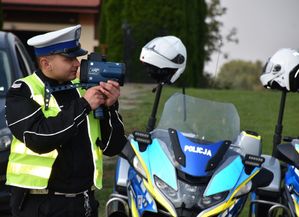 Policjant kontroluje prędkość. Obok niego znajdują się dwa policyjne motocykle