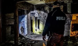 Pora nocna. Policjant kontroluje opuszczony budynek. Funkcjonariusz ma włączoną latarkę i oświetla pomieszczenie