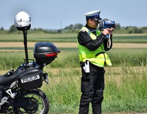 Policjant podczas pomiaru prędkości kierującego pojazdem. Obok policyjny motocykl