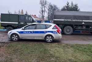 Pojazdy wojskowe- patrol saperski. Przed nimi znajduje się radiowóz