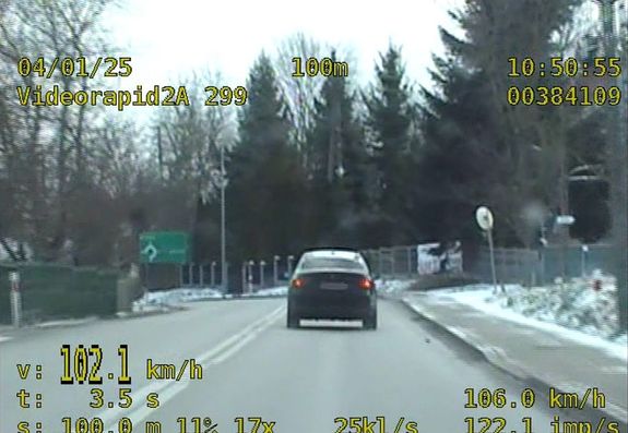 Zdjęcie z videorejestratora. Widoczna jest droga po której jedzie samochód osobowy. Czytnik videorejestratora wskazuje prędkość 102 km/h