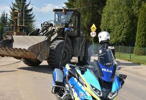 Policjant kieruje ruchem. Przed nim znajduje się policyjny motocykl
