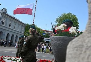 Część pomnika, przed nim salutujący żołnierz na tle flagi