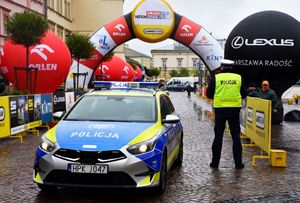 Policjant przy radiowozie. W tle balony oraz straty wyścigu kolarskiego