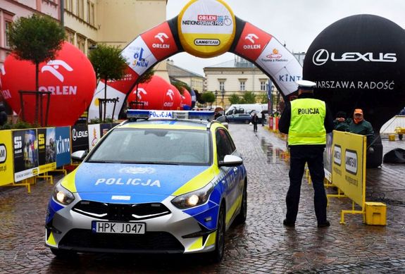 Policjant przy radiowozie. W tle balony oraz straty wyścigu kolarskiego