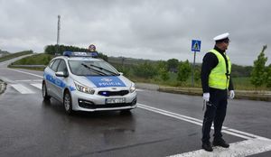 Policjant na drodze w czasie zabezpieczenia wyścigu kolarskiego. W tle radiowóz