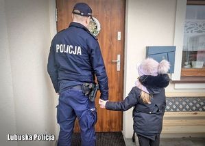 Policjant trzyma dziewczynkę za rękę. W tle wejście do mieszkania