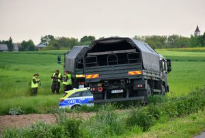 Pojazdy wojskowe na polach, pomiędzy nimi radiowóz