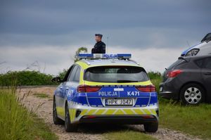 Radiowóz na drodze polnej. Za nim widoczny jest policjant