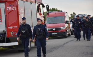 Policjanci przechodzą drogą. Obok wozy strażackie