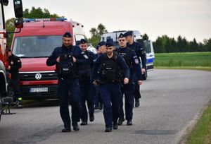 Policjanci idą drogą. Obok wóz strażacki