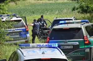 Radiowozy i pojazdy służbowe innych służb mundurowych,. W tle policjanci i pozorant