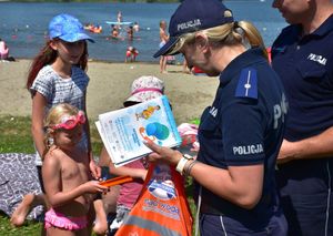Policjantka  na plaży rozdaje dzieciom informatory o bezpieczeństwie