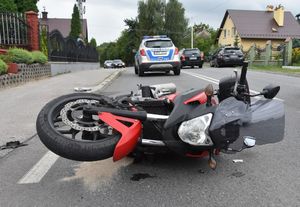 Miejsce wypadku drogowego. Na ulicy leży motocykl. W tle radiowóz i inne pojazdy