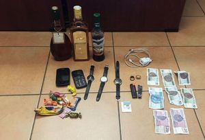 Na zdjęciu widoczne są rzeczy odzyskane przez policjantów tj. alkohol, telefony, sok malinowy, ładowarka, zegarki, banknoty oraz inne drobne przedmioty.