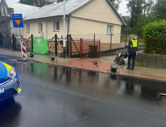 Miejsce wypadku drogowego. W tle policjant i uszkodzony motocykl