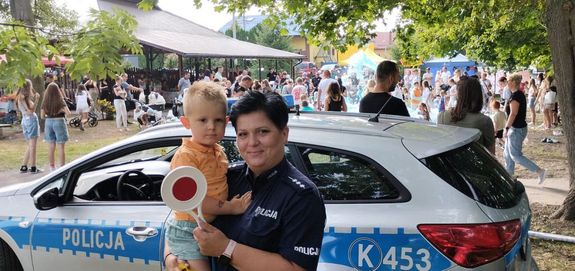 Policjantka z dzieckiem na rękach. W tle policyjny radiowóz