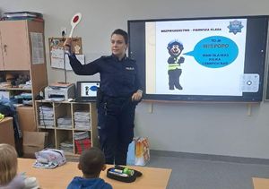 Policjantka pokazuje dzieciom tarczę sygnalizacyjną.