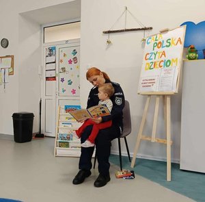 Policjantka trzyma na kolanach dziecko i czyta mu bajkę