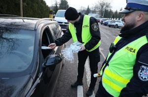 Funkcjonariusz Straży Miejskiej wręcza kierującemu pakiet profilaktyczny. Obok stoi policjant