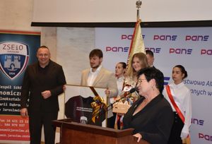 Kobieta przy mównicy. W tle poczet sztandarowy szkoły