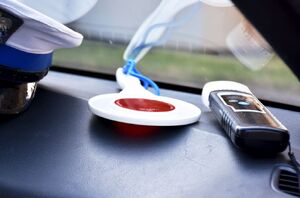 Zdjęcie przedstawia podszybie radiowozu na którym leżą; czapka policyjna, tarcza do zatrzymywania pojazdów oraz urządzenie do badania stanu trzeźwości kierujących.