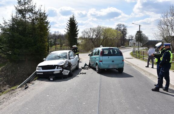 Wypadek drogowy. Na jezdni znajdują się dwa uszkodzone pojazdy. Obok nich stoją policjanci
